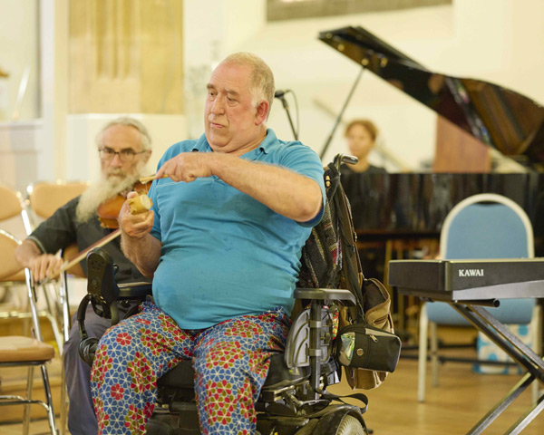 man in wheelchair playing instrument in music session with background piano and musicians