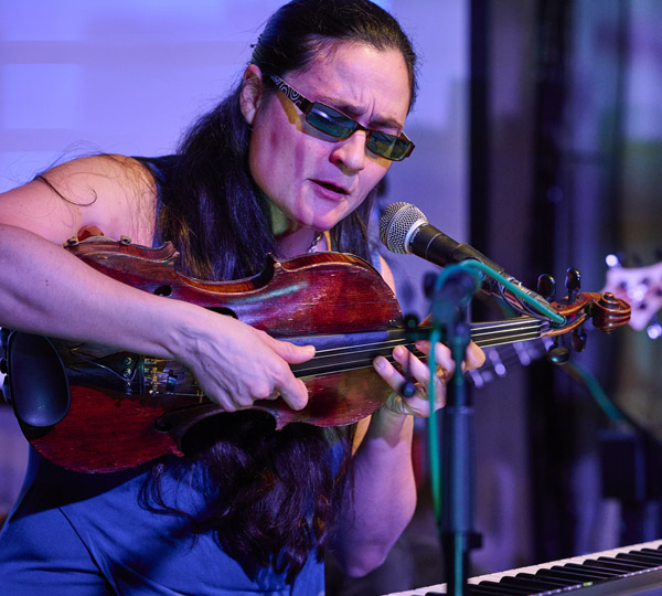 musician performing with violin singing on stage during live concert with three instruments in background