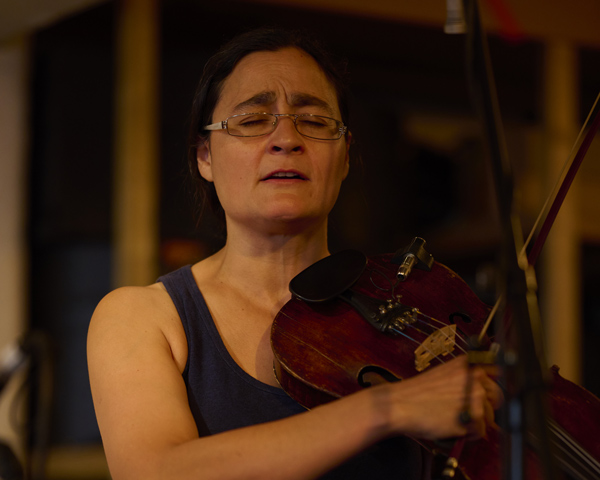 female musician playing violin with closed eyes performing music in a dimly lit space capturing the essence of music and emotion in the moment reflecting two passions